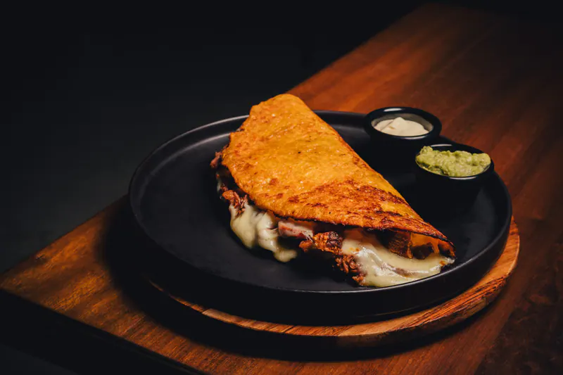 Arepa de chócolo paisa rellena de carne y queso fundido, en plato negro sobre tabla de madera