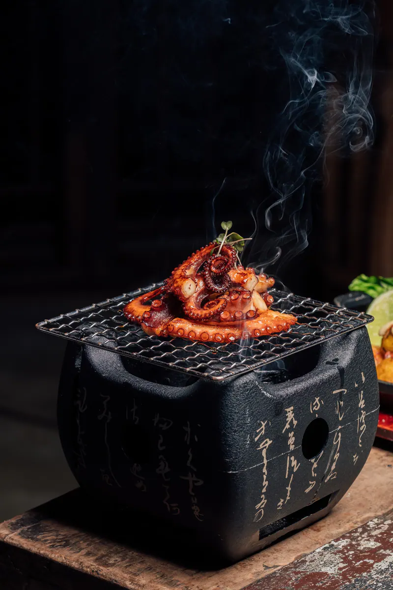 Robata de pulpo humeante sobre una parrilla japonesa de hierro